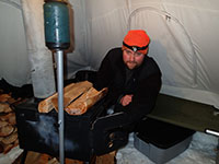 John Staying Warm by the Wood Stove in the Tent